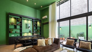 Una sala de estar moderna con una pared verde, un sofá marrón, una mesa de comedor y un ventanal grande.