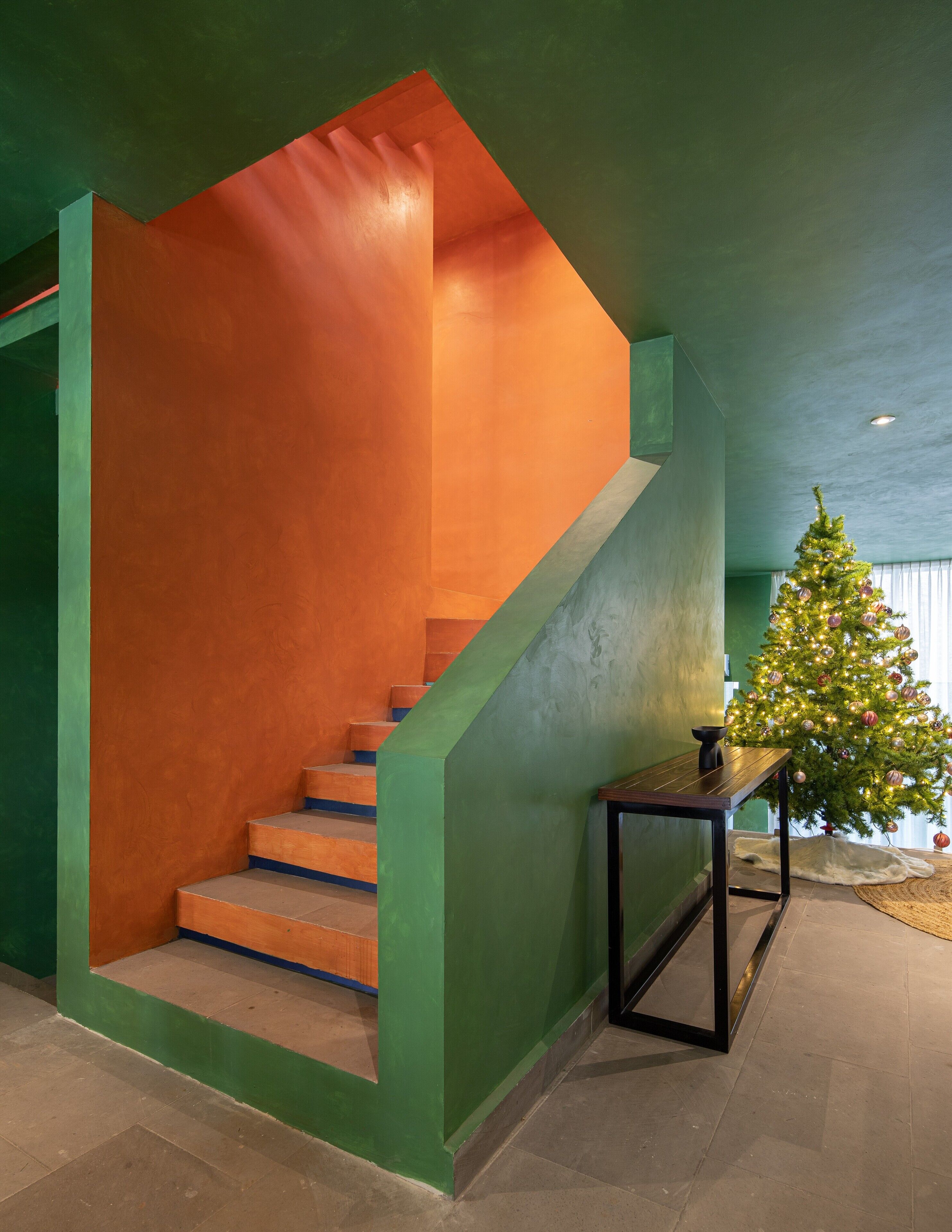A staircase with green walls and orange steps, a small table with a candle, and a decorated Christmas tree.