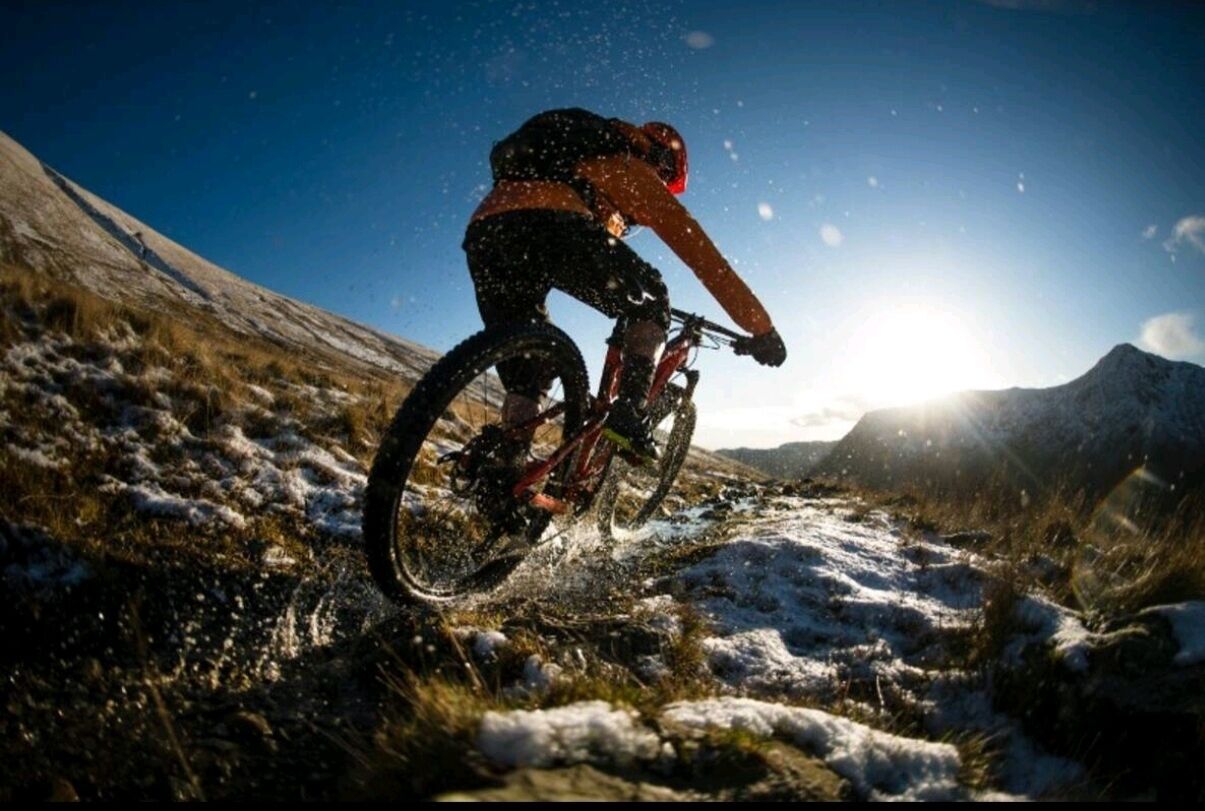 Eine Person fährt ein Mountainbike auf einem verschneiten Pfad vor einer Bergkulisse.