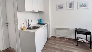 A compact kitchen with white cabinets, a stainless steel sink, and a blue kettle. There are three framed pictures on the wall and a small black table with books. - 1 bdr Apt, Kupres, centar, beautiful and uniqe plase (Kupres)