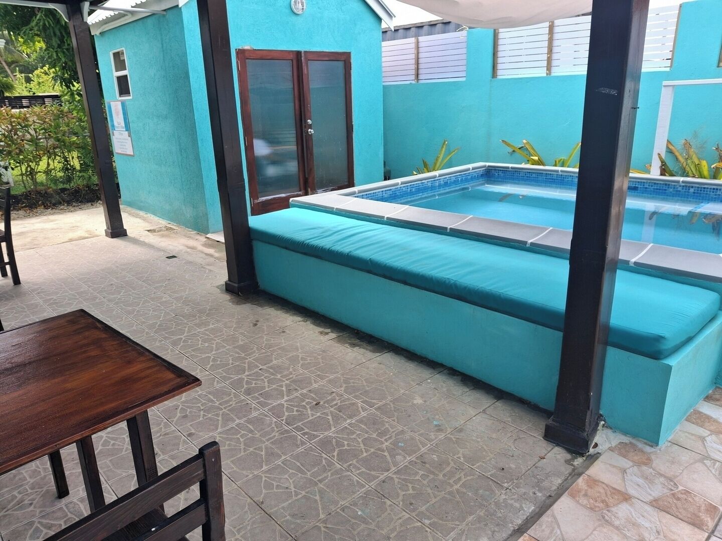 A swimming pool with a blue tiled deck, a wooden bench, and a table.