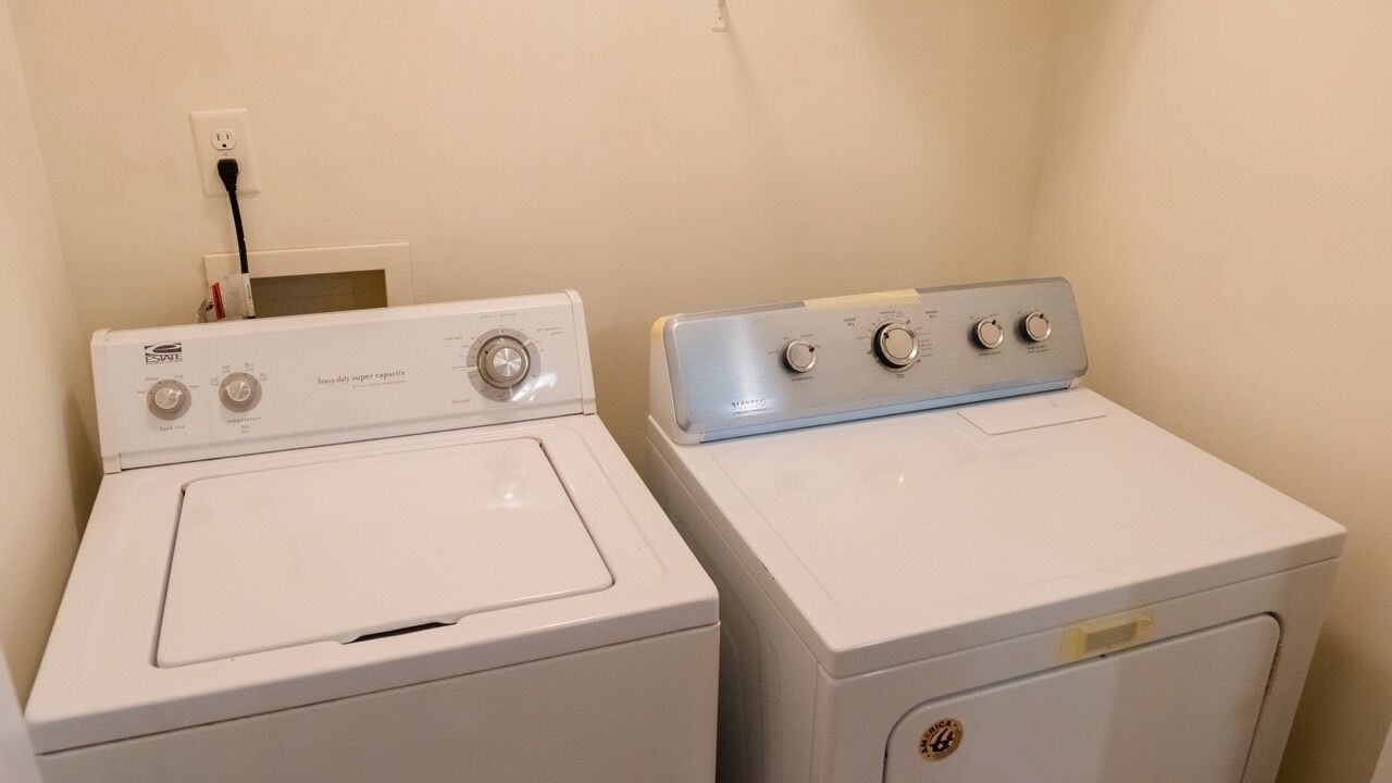Due lavatrici bianche in una lavanderia, con una presa di corrente e un quadro elettrico a parete.
