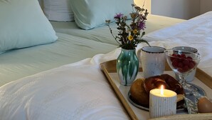 En snyggt bäddad säng med vita lakan och kuddar, ett bricka med mat och dryck samt en vas med blommor på ett nattduksbord.