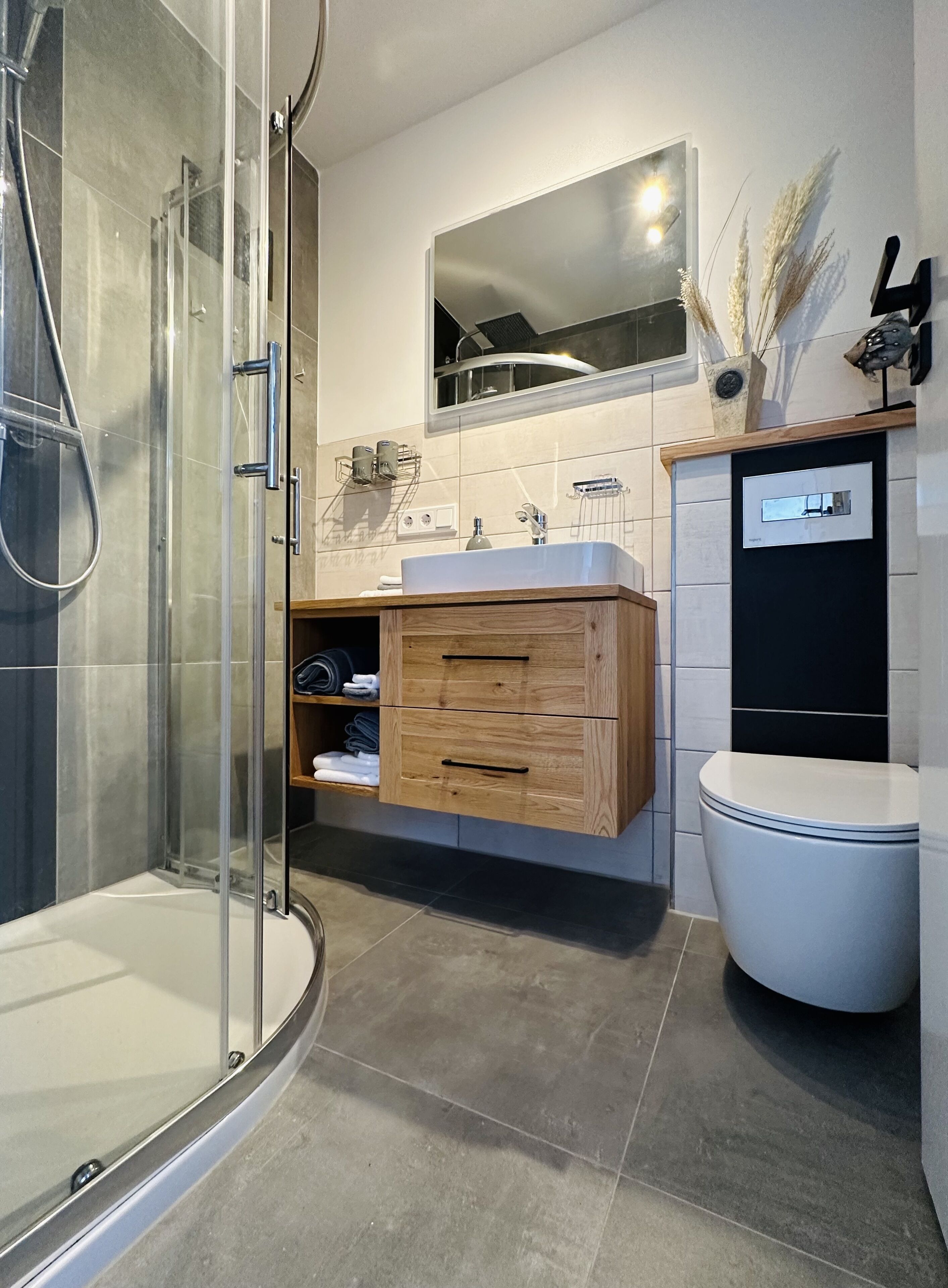 A modern bathroom with a glass shower enclosure, a wooden vanity with a sink, and a toilet.