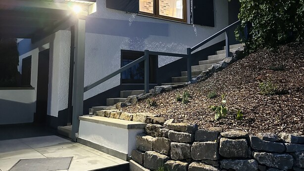 Ett modernt hus med en stentrappa som leder upp till entrén, en väl upplyst veranda och utsikt över det omgivande området.