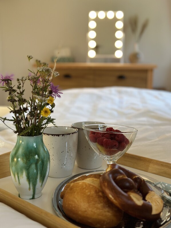 A tray with a green vase of flowers, a martini glass with raspberries, a pastry, and two mugs on a bed.