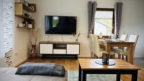 Ett modernt vardagsrum med en soffa, ett soffbord, en tv och en matplats med ett bord och stolar.