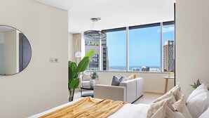 Une chambre d’hôtel moderne, dotée d’un grand lit, d’un canapé, d’une table à manger et offrant une vue sur le paysage urbain.