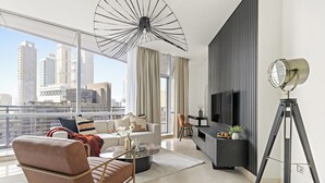 Un salon moderne avec un canapé, une table basse et un téléviseur. Une grande fenêtre offre une vue sur la ville.