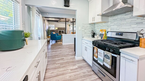 A modern kitchen with white cabinets, a stainless steel range, and a wooden floor.