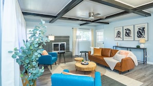 A modern living room with a sofa, armchairs, a coffee table, and a television. There is a ceiling fan, a plant, and artwork on the wall.