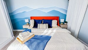 A bedroom with a bed, two nightstands, a wall mural, and a window with curtains.