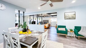 A modern living room with a dining area, a ceiling fan, and a large window.