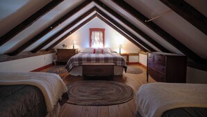 Un dormitorio en el ático con techo inclinado, una cama con colcha escocesa, dos mesitas de noche con lámparas, un aparador y una ventana con cortinas.