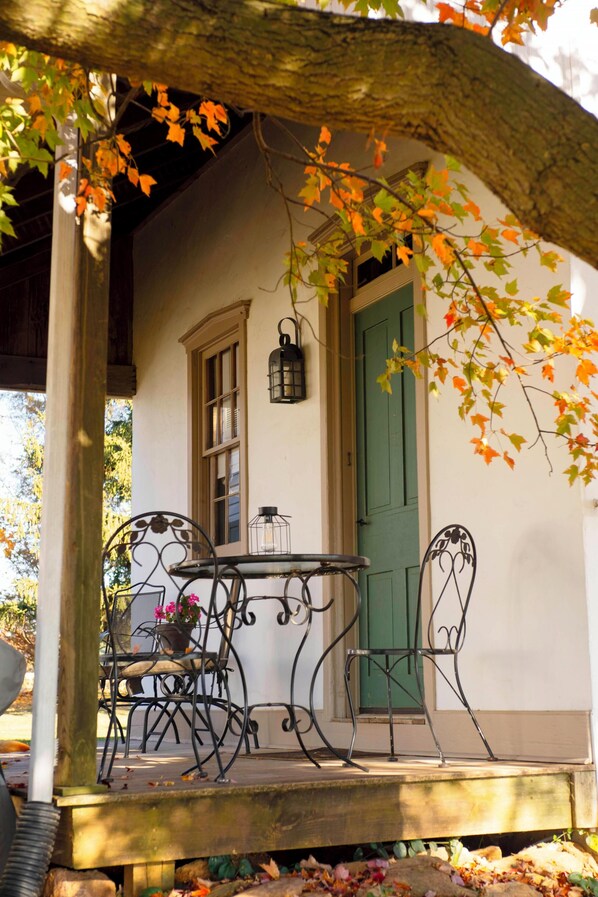 Un porche abrité avec une table et des chaises, une porte verte et une lanterne suspendue.