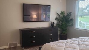 A bedroom with a bed, a dresser, a mirror, and a window with blinds.