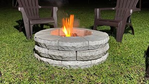 A stone fire pit with a fire burning in the center, surrounded by two Adirondack chairs. - Charming, beautiful cabin. (La Fortuna)