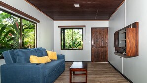 A living room with a blue sofa, wooden coffee table, and a TV mounted on the wall. - Charming, beautiful cabin. (La Fortuna)