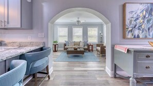 Une cuisine moderne dotée d’un plan de travail en marbre, de chaises recouvertes de tissu bleu, d’une table basse centrale et d’un coin repas avec une table et des chaises.