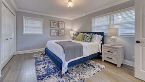 Une chambre à coucher comprenant un lit, des tables de chevet, une commode, une fenêtre avec des stores et un luminaire au plafond.