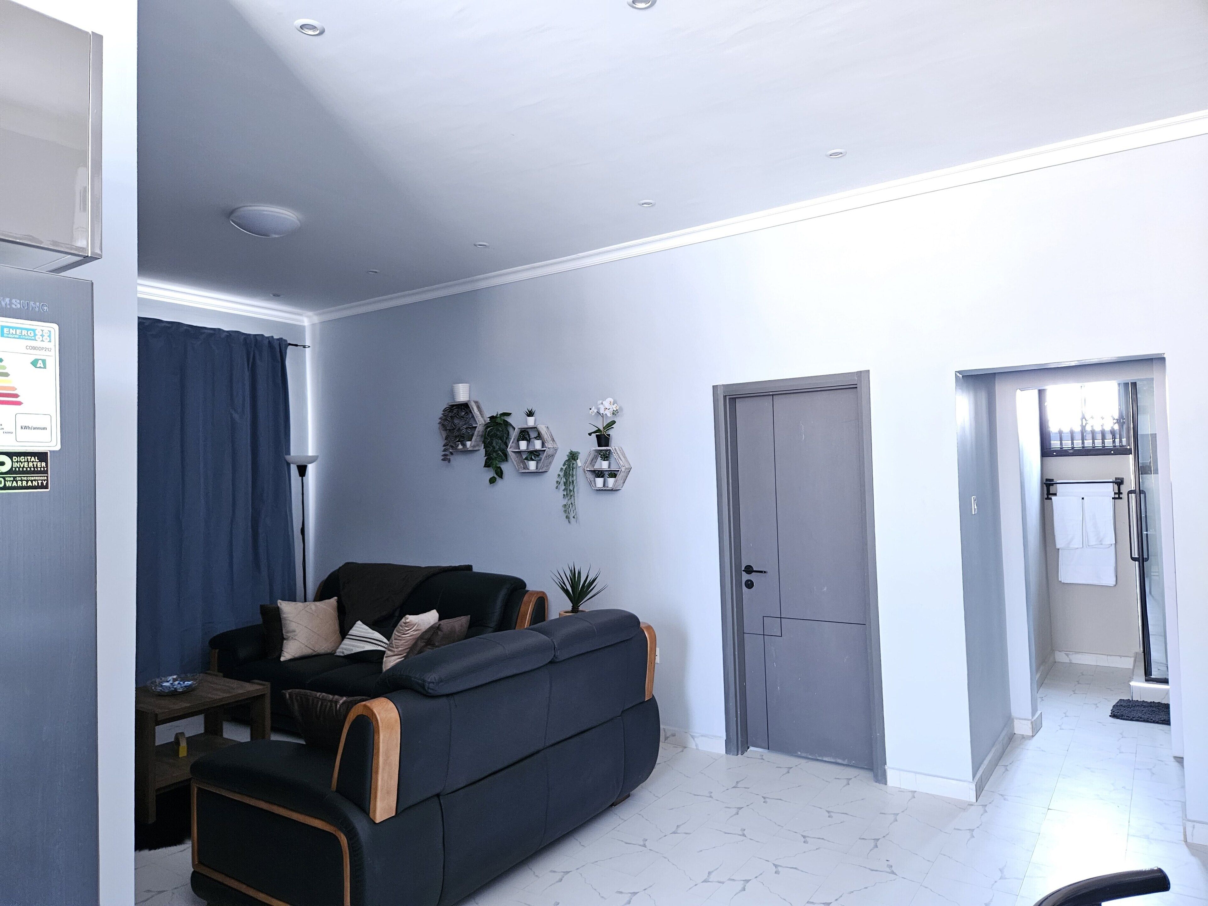 Un salon moderne avec un canapé foncé, une petite table et une porte donnant sur une salle de bain.