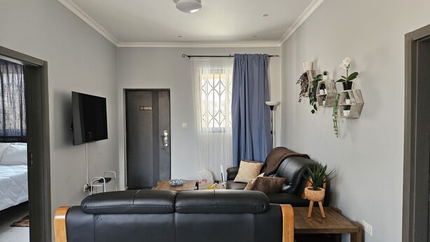 Una sala de estar moderna con un sofá de cuero negro, una mesa de centro de madera y un televisor montado en la pared.