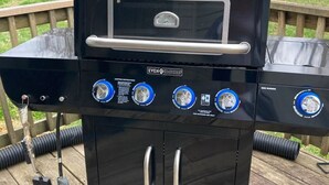 Een zwarte barbecue met een digitaal display, vier bedieningsknoppen en een extra brander.