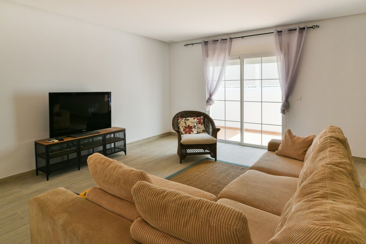 Una sala de estar con un sofá, un televisor, una silla y una ventana con cortinas.