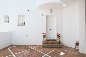 A clean, white-walled interior with a tiled floor, a door with a small window, and two potted plants with red flowers. - Spectacular House. Ocean Vistas (Benalmádena)