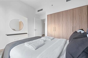 A modern bedroom with a large bed, a wooden wardrobe, a round mirror, and a bedside table.