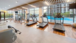 A modern gym with treadmills, weight machines, and a large window overlooking a swimming pool. - Silkhaus Executive Residences, Dubai Hills (Dubai)