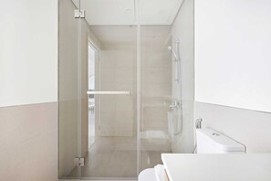 A modern bathroom with a glass shower enclosure, a white sink, and a visible door leading to another room.
