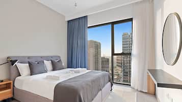 Quarto de hotel moderno com uma cama grande, mesa de cabeceira, espelho e vista da cidade através de uma janela ampla.