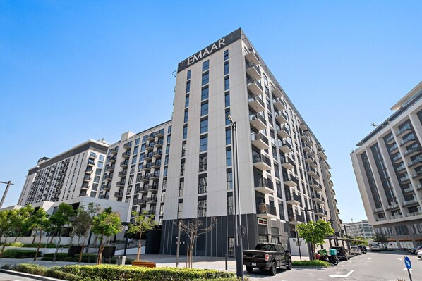 A multi-story building with the name 'EMAAR' on the facade, surrounded by greenery and a clear sky.