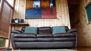 Un interior de madera con un sofá de cuero marrón, un cuadro en la pared y un estante con altavoces.