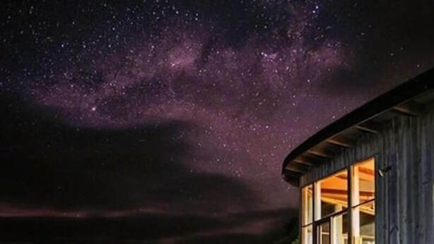 Una cabaña de madera con ventanas amplias bajo un cielo estrellado.
