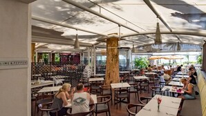 An outdoor dining area with tables and chairs, a large tree, and a sign reading 'LIME & PEPPER'.