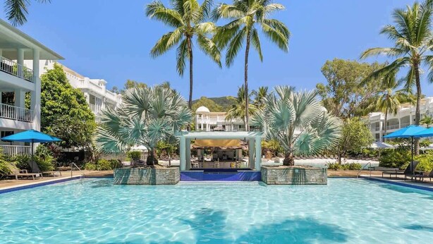 A swimming pool with a central bar area, surrounded by palm trees and lounge chairs.
