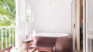 A bathroom with a wooden bench, a bathtub, and a window with blinds.