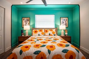 A bedroom with teal walls, a floral bedspread, two bedside lamps, and artwork on the walls.