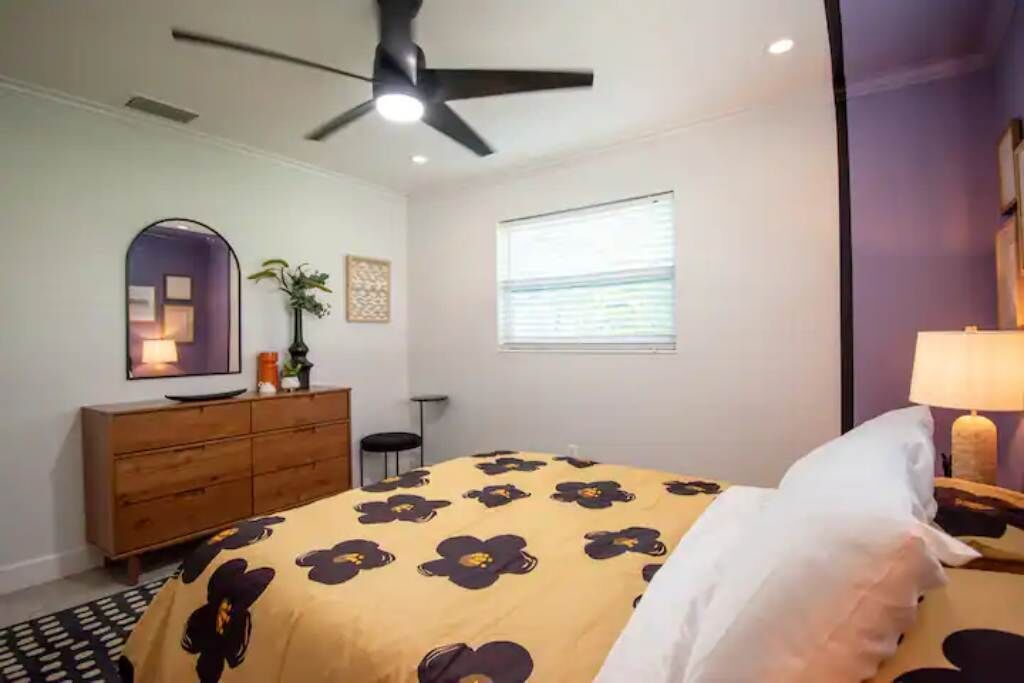 A bedroom with a bed, a ceiling fan, a dresser, a window, and a nightstand.