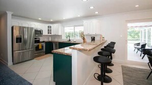 Cozinha moderna com eletrodomésticos de aço inoxidável, bancada de granito e um balcão com banquetas.