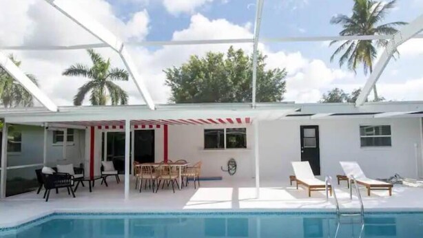 Uma área de piscina com espreguiçadeiras, mesa e um espaço coberto para sentar.