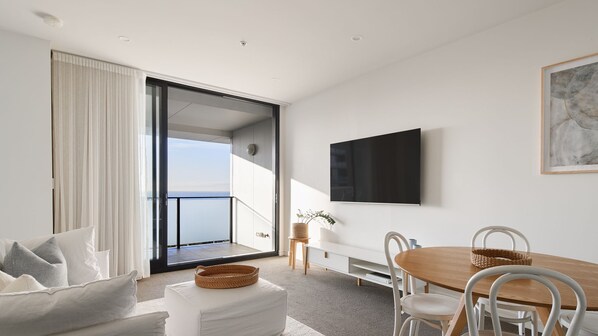 A modern living room with a balcony, a dining area, and a flat-screen TV mounted on the wall.