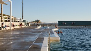 Une promenade en bord de mer dotée d’une piscine, d’espaces aménagés pour s’asseoir et offrant une vue sur la mer.
