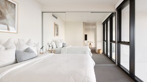 Une chambre d’hôtel avec deux lits, une grande fenêtre et un couloir menant à une autre chambre.