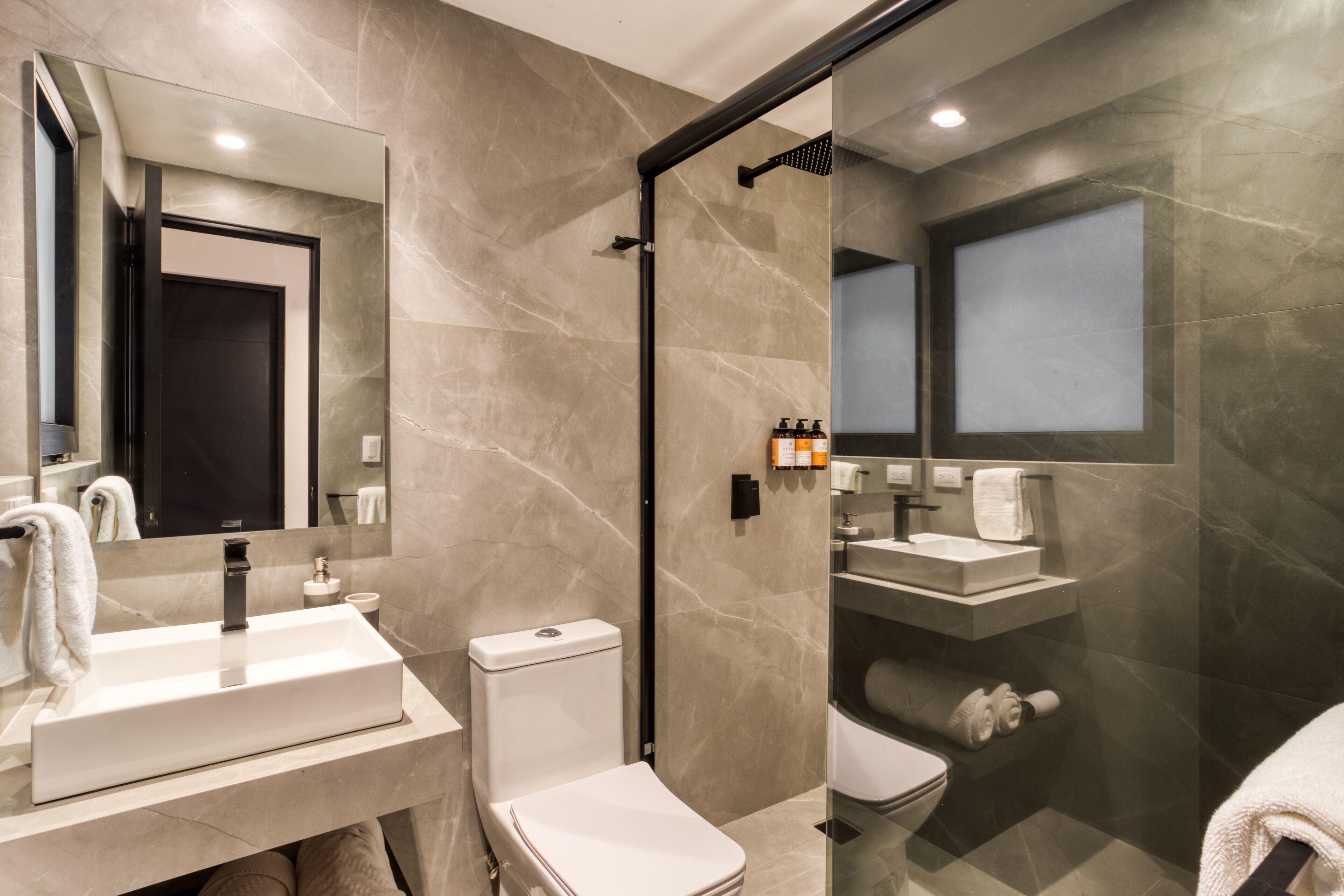 Un baño moderno con ducha de vidrio, lavamanos blanco y retrete.