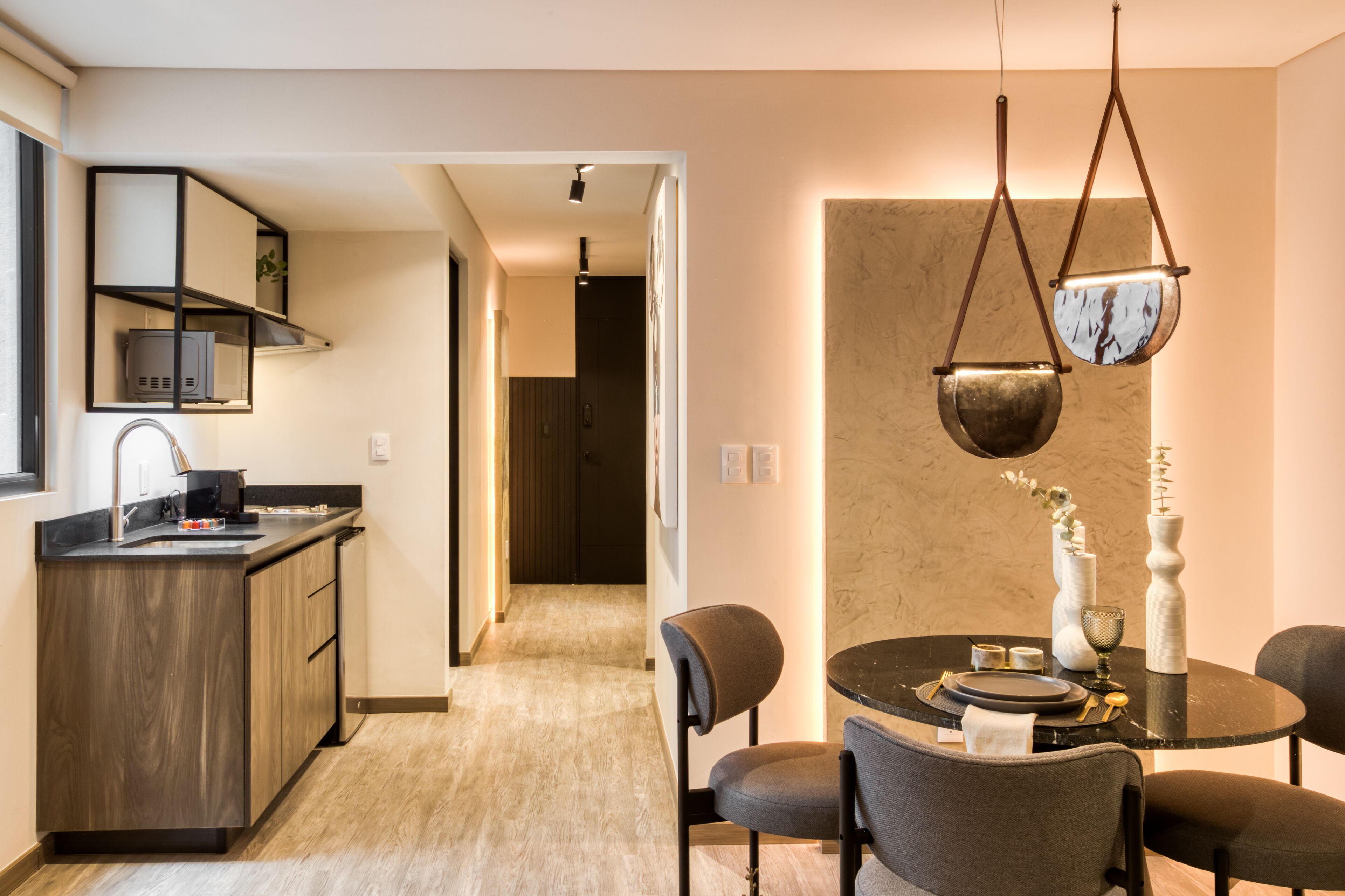 A modern kitchen with dark wood cabinets, a built-in microwave, and a black countertop. There is a dining area with a round table, chairs, and a vase with flowers.