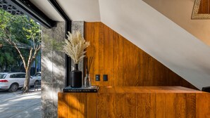 Una recepción con encimera de madera y base de piedra, un jarrón con plumas de mispolonia, y un cartel que dice "VOGUE LOCATION".