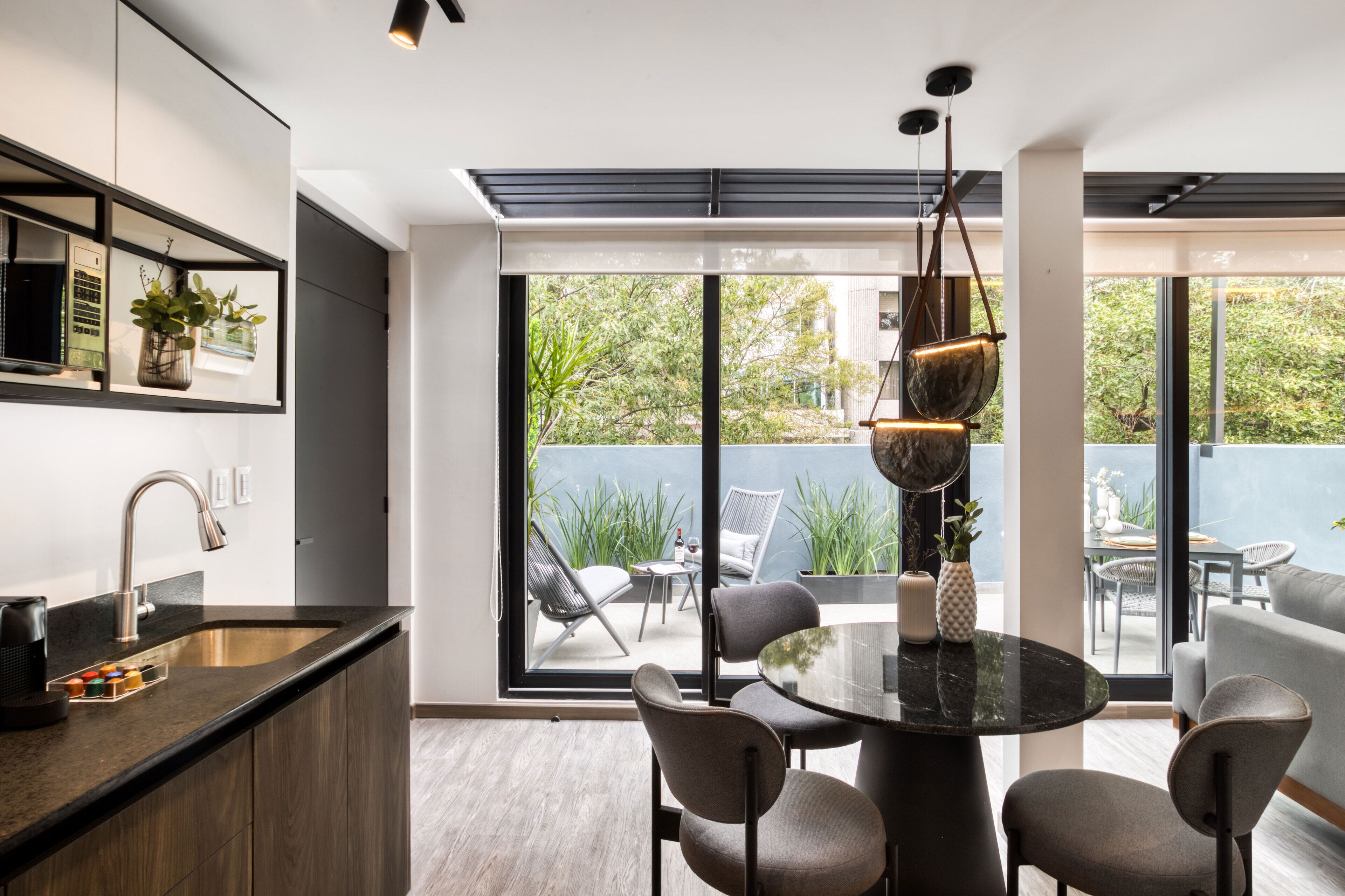 Una cocina moderna con un amplio ventanal, un comedor con mesa redonda y un balcón con mobiliario exterior.